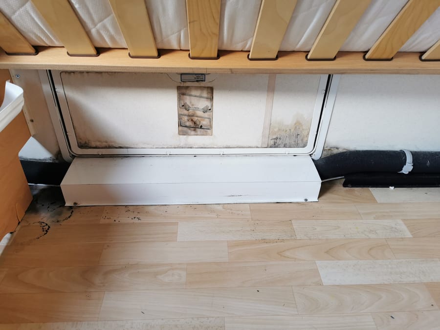 Sort skimmel langs kanten af en serviceluge set indefra under en seng i en campingvogn